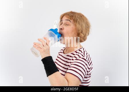 Ältere Frau trinkt Wasser, während sie auf weißem Hintergrund trainiert. Stockfoto