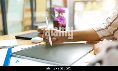 Nahaufnahme, weibliche Hand mit Eingabestift zum Zeichnen auf Grafik-Tablet am gemütlichen Arbeitsplatz Stockfoto