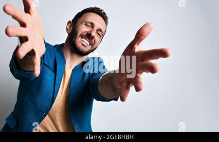 Porträt eines freundlich lächelnden erwachsenen Mannes in legerer blauer Jacke und gelbem T-Shirt, der seine Hände ausstreut, die Finger ausgebreitet Stockfoto