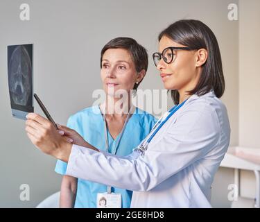 Zwei verschiedene Ärztinnen in Uniform betrachten die Hirntomographie und diskutieren die Diagnose Stockfoto
