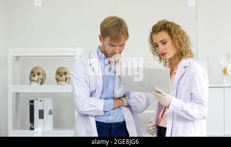 Die junge blonde Wissenschaftlerin und ihre Assistentin betrachten die Forschungsergebnisse auf dem Clipboard. Arbeitsatmosphäre im orthopädischen Labor Stockfoto
