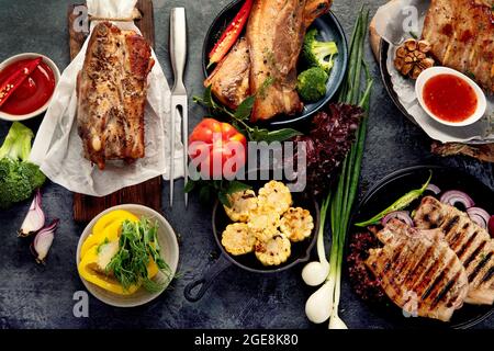 Auswahl an gegrilltem Schweinefleisch mit Gemüse auf dunkelgrauem Hintergrund. Bio-Gourmet-Food-Konzept. Draufsicht, flach liegend Stockfoto