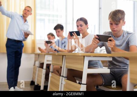 Klassenkameraden nutzen ihre Smartphones während der Nahaufnahme des Unterrichts stark Stockfoto