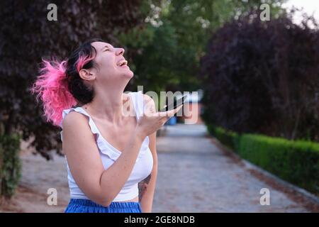 Junge kaukasische Frau mit rosafarbenem Haar lachend, während sie eine Audionote aufzeichnete. Stockfoto