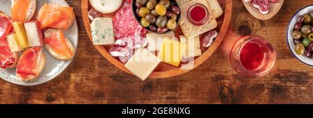 Panorama aus Wurstwaren und Käseplatten mit Rosenwein, Oliven und einem Platz für Text, aufgenommen von oben auf rustikalem Hintergrund. Spanische Tapas oder italienische Antipasti Stockfoto