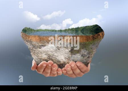 Menschliche Hand hält unterirdische Bodenschicht von Querschnitt Erde mit See und Hügeln auf der Oberseite mit farbigem Hintergrund Stockfoto