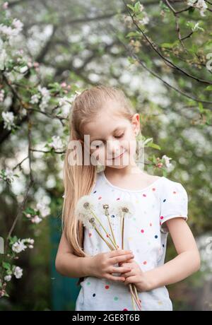 Kleines Mädchen in einem Frühlingsgarten mit weißen Dandelionen in ihren Händen Stockfoto