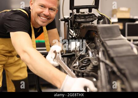 Lächelnder Schlosser, der im Servicezentrum Motorrad mit Schraubenschlüssel repariert Stockfoto
