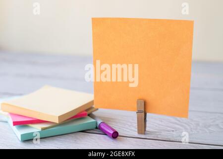 Unbeschriftete Haftnotiz Mit Laundry Clip Stapel Farbenfroher Papierschreiber Auf Dem Tisch. Leeres Blatt Wurde Neben Stift Und Auffälligen Papieren Auf Dem Schreibtisch Abgeschnitten. Stockfoto