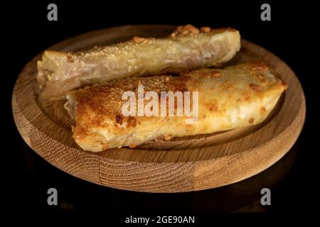 Zwei hausgemachte Mini-Apfelstrudel auf einem runden Holztablett, Nahaufnahme, isoliert auf Schwarz. Stockfoto