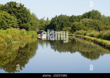 Ein Narrowboot passiert ein verankertes Breitstrahl-Boot auf einer Kurve in der Nähe von Burscough am Leeds & Liverpool Kanal Stockfoto