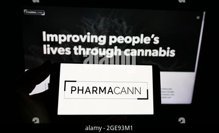 Person, die ein Smartphone mit dem Logo des US-Cannabisunternehmens PharmaCann Inc. Auf dem Bildschirm vor der Website hält. Konzentrieren Sie sich auf die Telefonanzeige. Stockfoto