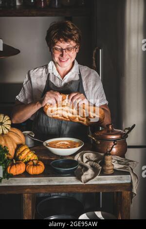 Frau schneidet Brot für die Herbstsuppe mit Kürbiscreme Stockfoto