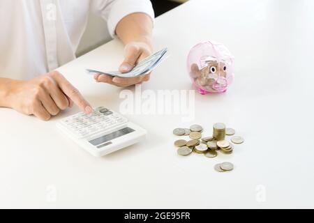 Ein Mann verwenden Rechner und halten das Geld in der Nähe von Gruppe von Münzen auf dem weißen Tisch Konzept Geschäft Geld sparen. Stockfoto