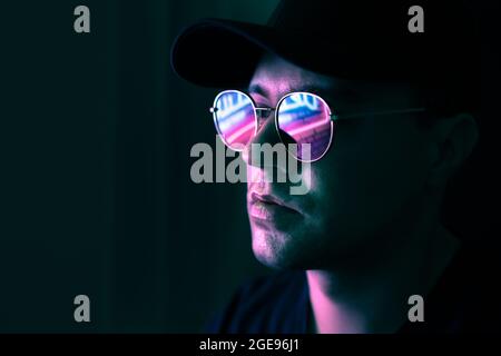 Neonspiegelung in der Brille. Mann in fluoreszierendem Licht aus der Stadt führte Zeichen. Geheimnisvolles cooles Modell im futuristischen Cyberpunk-Portrait. Mann in Sonnenbrille. Stockfoto