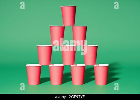 Pyramide aus roten Pappbechern auf grünem Hintergrund. Minimalismus-Konzept Stockfoto