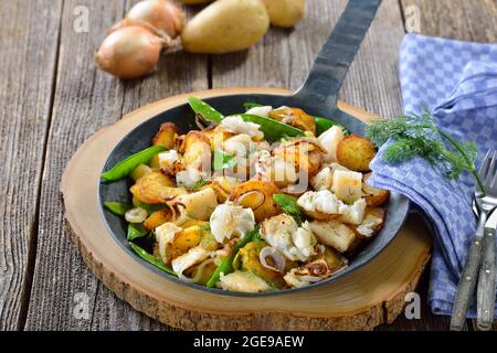 Gebratene Kartoffeln mit Halibutfilet, Zuckererbsen und Zwiebelringen, oft in einer Pfanne serviert Stockfoto