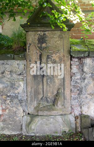 Ein barocker Grabstein mit dem gekreuzigten Jesus in der Friedhofsmauer Stockfoto