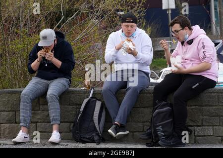 Luzern, Schweiz 04 17 2021: Drei Jugendliche essen vor einem Restaurant zum Mitnehmen. Sie sitzen in der Innenstadt von Luzern, Schweiz. Sie Stockfoto