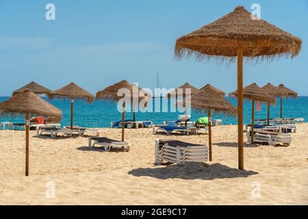 Blick auf den Luxusstrand am Meer mit Liegestühlen und Sonnenschirmen, in der touristischen Zone der Tropen. Im Hintergrund ist ein Yacht-Segelschiff. Stockfoto