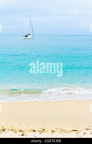 Segelboot an der Küste vor Anker, türkisfarbenes Wasser und gelber Sandstrand, Kopierraum, Hintergrundstruktur im aufrechten Format. Stockfoto