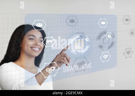 Glückliche afroamerikanische Frau, die Hausfunktionen über virtuelle Konsole steuert Stockfoto