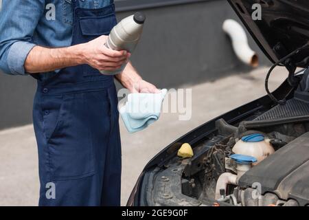 Beschnittene Ansicht eines Mechanikers, der eine Flasche Poliermittel und einen Lappen in der Nähe des Autos hält Stockfoto