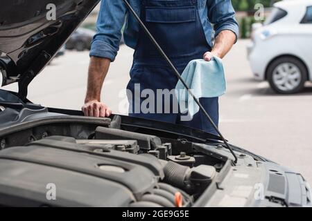 Beschnittene Ansicht eines mechanischen Lappens in der Nähe des Autos mit offener Haube im Freien Stockfoto