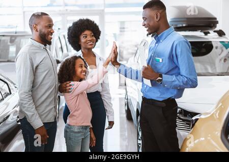 Schöne schwarze Mädchen hoch fiving freundlichen Verkäufer bei Autohaus Stockfoto