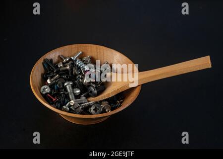 Kleine bunte Schrauben in einer Holzschale mit einem Löffel, isoliert auf schwarz Stockfoto