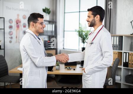 Gute Arbeit, Gut gemacht. Healthcare und professionelle Arbeit Konzept, wo zwei lächelnde qualifizierte arabische Ärzte in der Klinik geben einen Händedruck zueinander, Erfolg und Vereinbarung zu feiern. Stockfoto