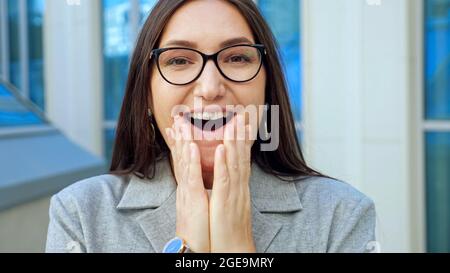 Die junge Frau in der Brille lächelt überrascht vor der Kamera und tanzt Stockfoto