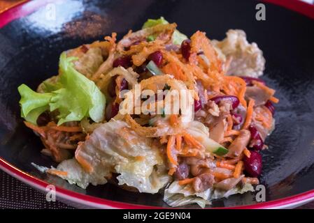 Köstlicher asiatischer Salat auf einem schwarzen Teller. Rote Bohnen, Fleisch, Salat und andere Zutaten. Stockfoto