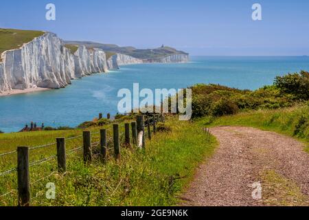 Blick auf den Pfad zu den Cottages der Küstenwache mit den Seven Sisters und dem Leuchtturm Belle Tout in der Ferne. Stockfoto