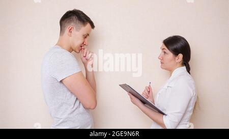 Ärztin im Gespräch mit einem männlichen Patienten und füllt ein Dokument aus, wobei Anamnese Stockfoto