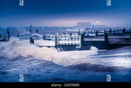 Wellen brechen am Strand und buhnen in Southwold mit Sizewell Kernkraftwerk in der Ferne. Stockfoto