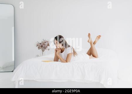 Entzückende Frau, die mit Stift und Tagebuch im Bett liegt. Stockfoto