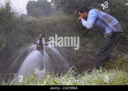 Landwirtschaftliche Ausrüstung für die Feldbewässerung, ein indischer Landwirt Trinkwasser aus Wasserstrahl überfließt auf seiner Farm, Regennebel, selektiver Fokus Stockfoto