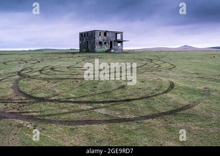 Reifenspuren im Gras, die Joy Riders vor dem verletzten Kontrollturm auf dem nicht mehr genutzten WW2 RAF Davidstow Airfield auf Bodmin Moor in Cornwall hinterlassen hat. Stockfoto