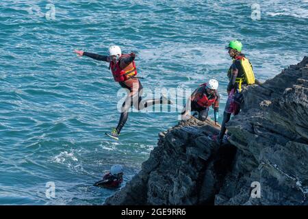 Urlauber, die von Felsen springen und mit einem Fremdenführer auf Towan Head in Newquay in Cornwall herumlaufen. Stockfoto