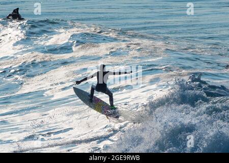 Ein Surfer, der einen Lufttrick auf einer Welle in der Fistral Bay in Newquay in Cornwall macht. Stockfoto