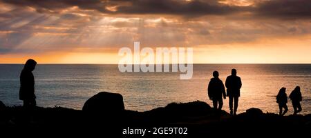 Ein Panoramabild der Wanderer auf dem Küstenpfad, der von einem spektakulären Sonnenuntergang über der Fistral Bay in Newquay in Cornwall umragt wird. Stockfoto