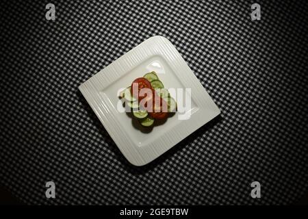 Ein veganes Sandwich mit Gurken und Tomaten auf einem weißen Teller. Stockfoto