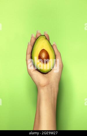 Crop unkenntlich weiblich demonstriert köstlich geschnitten reife Avocado mit weichem Fruchtfleisch auf hellgrünem Hintergrund Stockfoto