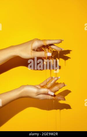 Crop unkenntlich weiblich zeigen Hand mit Maniküre und aromatischen Honigflüssigkeiten auf gelbem Hintergrund mit Schatten Stockfoto