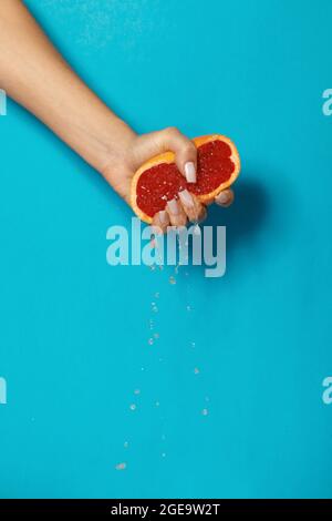 Crop anonyme weiblich mit Maniküre quetschen die Hälfte der frischen reifen saftigen Grapefruit vor blauem Hintergrund Stockfoto