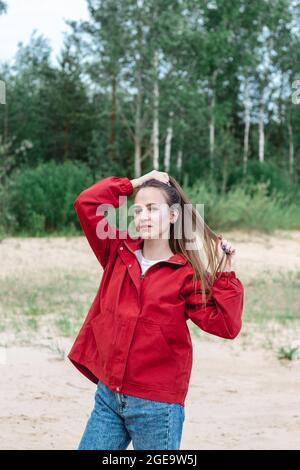 Auffallendes Porträt einer jungen kaukasischen Frau in roten Kleidern, die mit ihren Haaren spielt und posiert Stockfoto