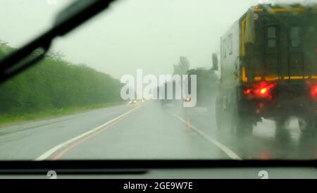 Säule moderner Militärfahrzeuge auf der Autobahn. Unschärferer Verkehr, der durch eine regenbedeckte Autoscheibe betrachtet wird. Das ist im Herbst Stockfoto