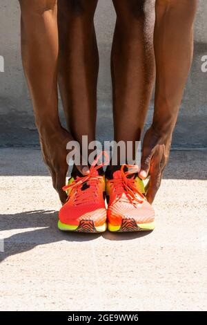 Crop unkenntlich afroamerikanischen männlichen Athleten in lebhaften Turnschuhen tun vorwärts beugen und Strecken Beine während des Trainings an sonnigen Tag in der Stadt Stockfoto