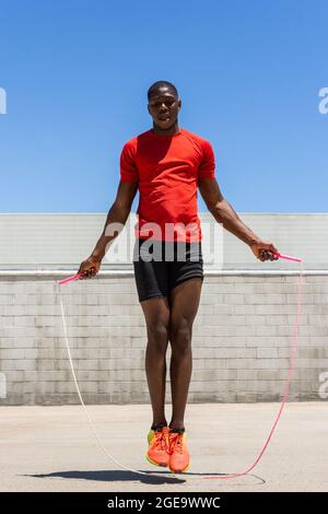 Energischer afroamerikanischer Athlet, der im Sommer beim Training Seil über den Boden hüpft Stockfoto